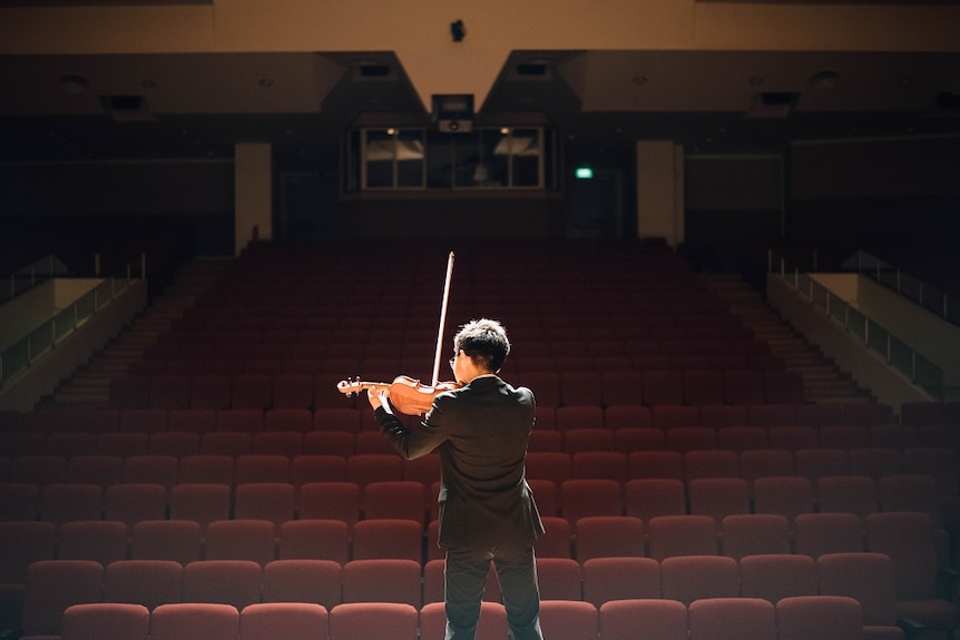 A man standing in front of an empty room to play the violin