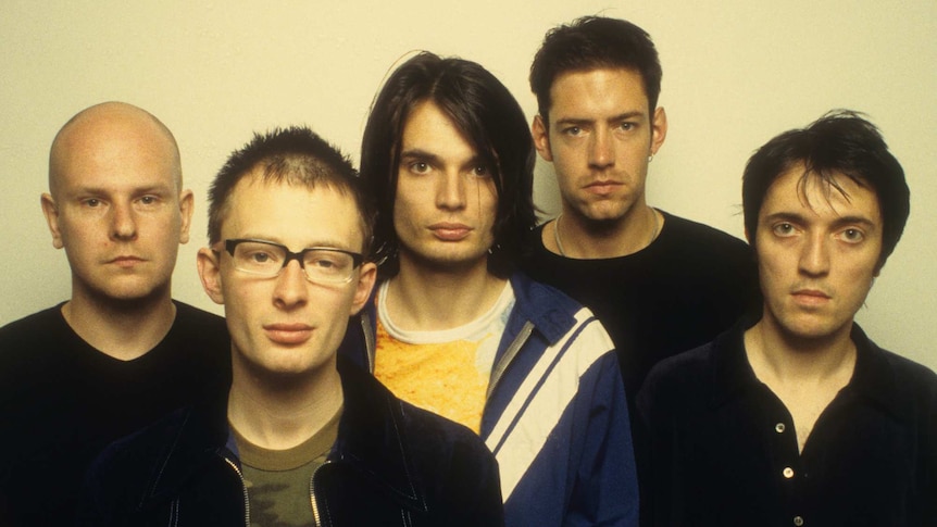 Five members of Radiohead stare deadpan at the camera. They stand before a plain yellow wall.