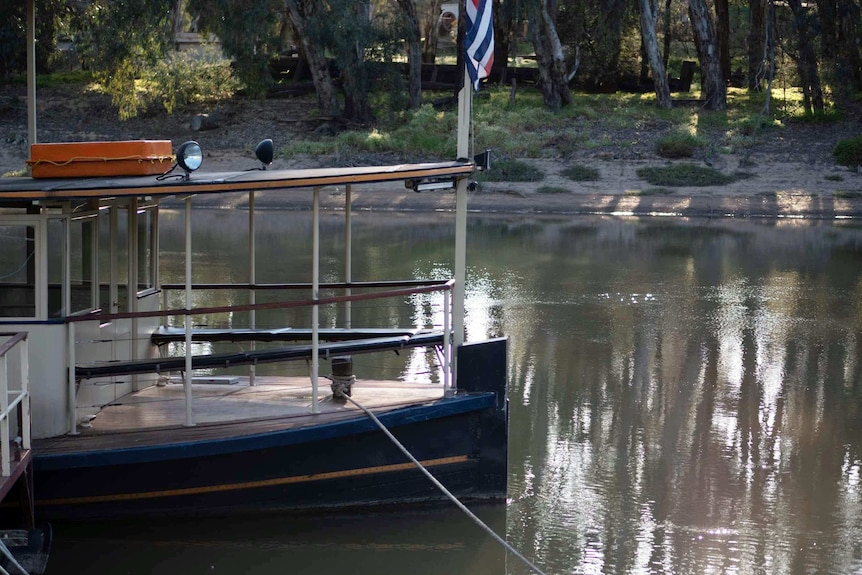 a paddle steamer sits empty and idle on still and glassy water.