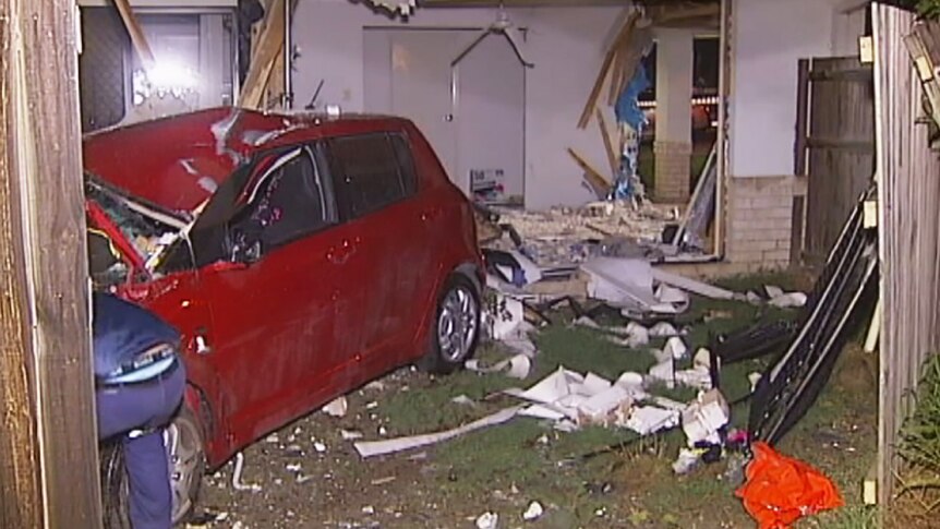 A smashed car at the back of a house it has driven through