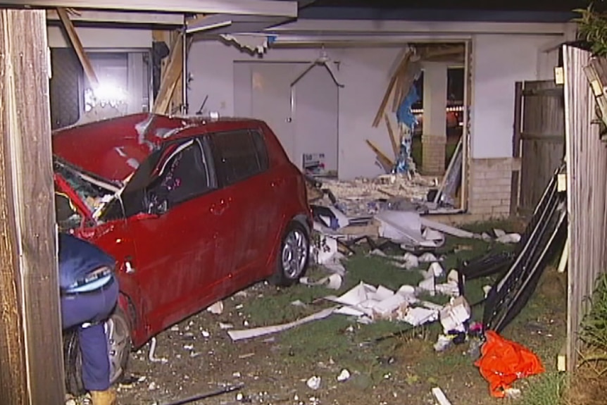 A smashed car at the back of a house it has driven through