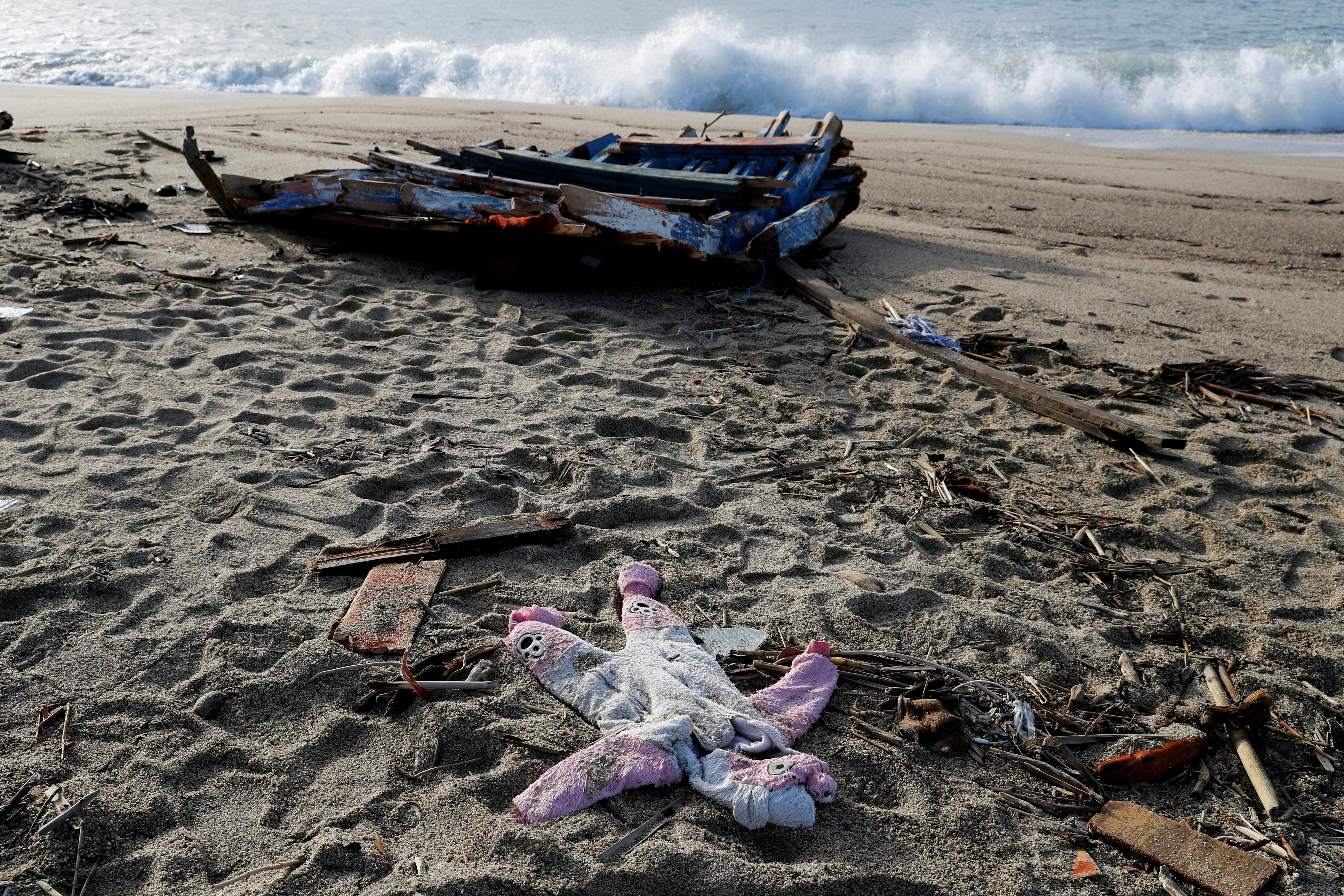 A pink clothing lays on the beach in front a boat wreck. 