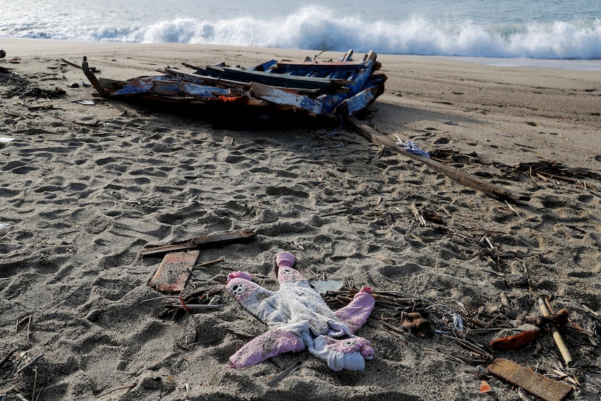 A pink clothing lays on the beach in front a boat wreck. 