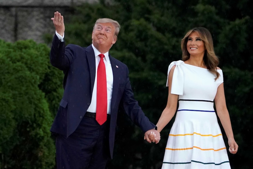 Donald Trump holds his hand up to the sky while walking next to his wife Melania
