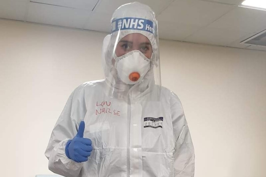 Louise Faint, wearing PPE gear that covers her entire body, gives a thumbs-up.