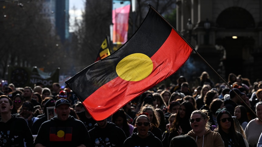 a large aboriginal flag flying above a large group of people at a city march