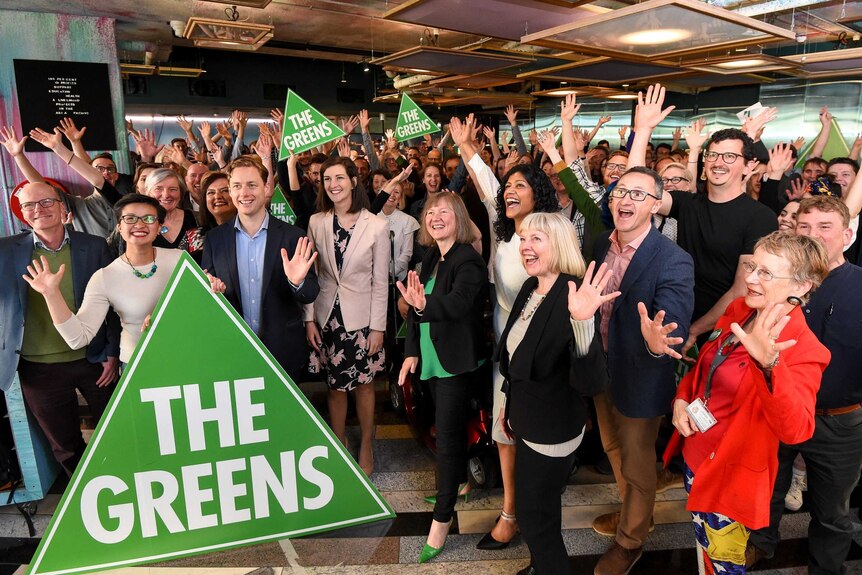 A group of people smiling and waving with several holding a sign saying The Greens.