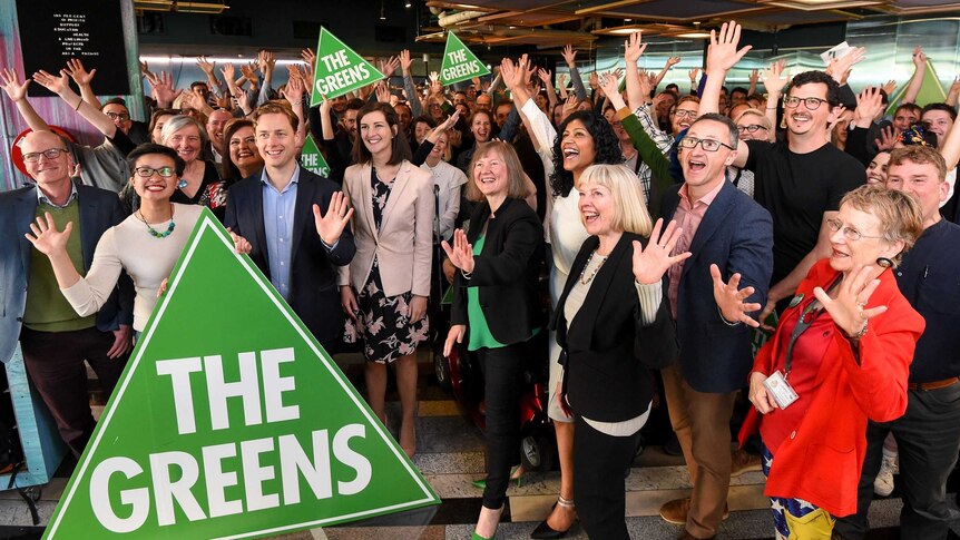 A group of people smiling and waving with several holding a sign saying The Greens.