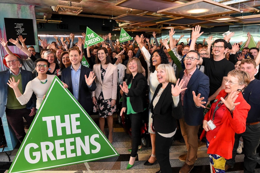 A group of people smiling and waving with several holding a sign saying The Greens.