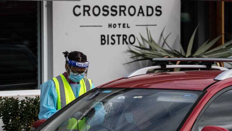 A health worker in PPE testing someone in a car outside the Crossroads Hotel.