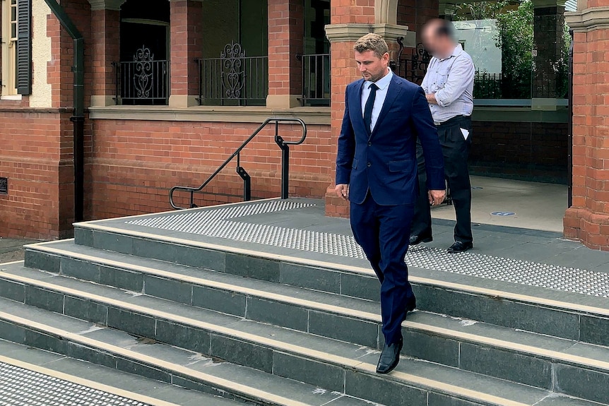 A man in a blue suit walks down steps in front of a red brick building.