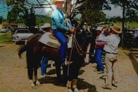 A grainy shot of a man dressed in cowboy gear sitting astride a horse.