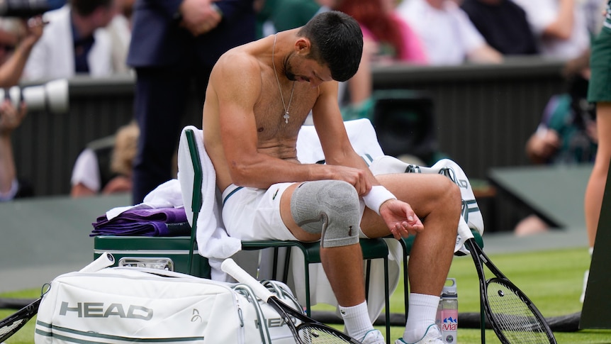 Novak Djokovic sits shirtless with his head down on a chair at Wimbledon.