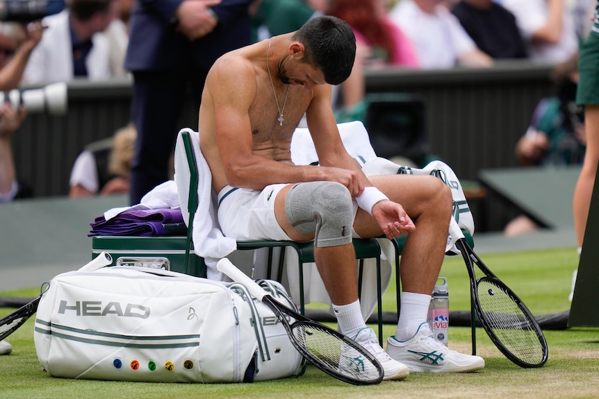 Novak Djokovic sits shirtless with his head down on a chair at Wimbledon.
