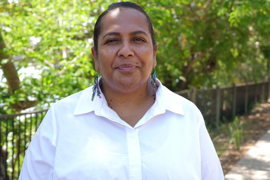 A woman, with a leafy background, smiles into the camera