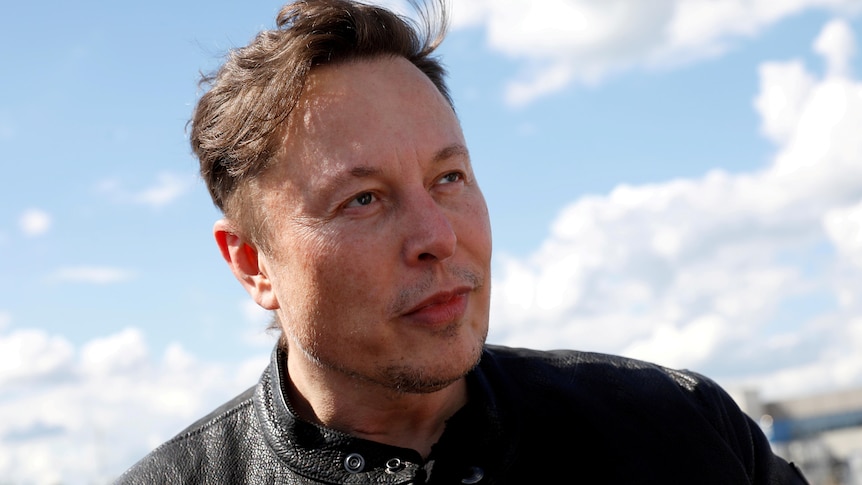 Elon Musk in a black leather jacket with sky and clouds behind