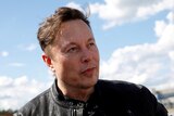 Elon Musk in a black leather jacket with sky and clouds behind