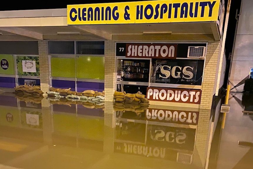 Sandbags at the front door of a cleaning shop, keeping back brown floodwater.