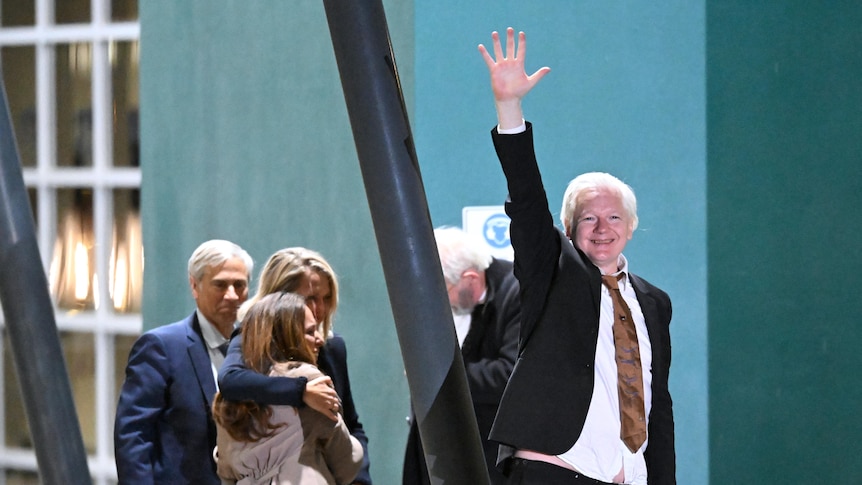 Julian Assange smiling and waving. 