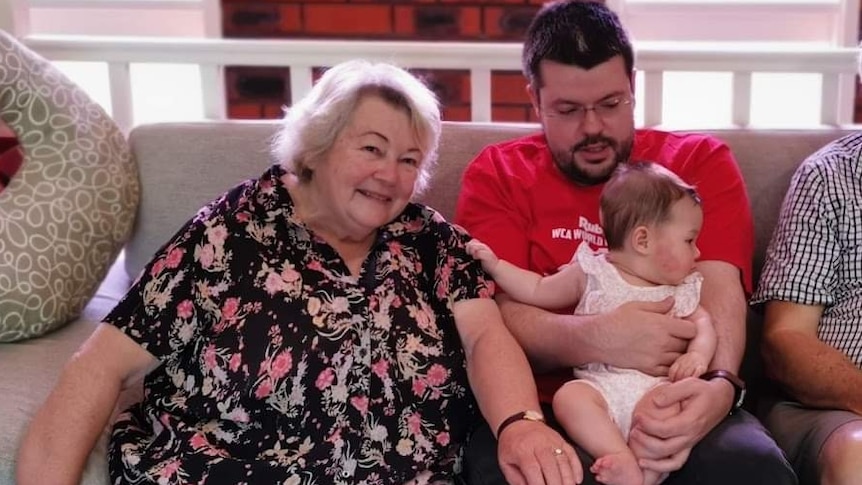 A woman and a man sit on a bench. The man is holding a baby.