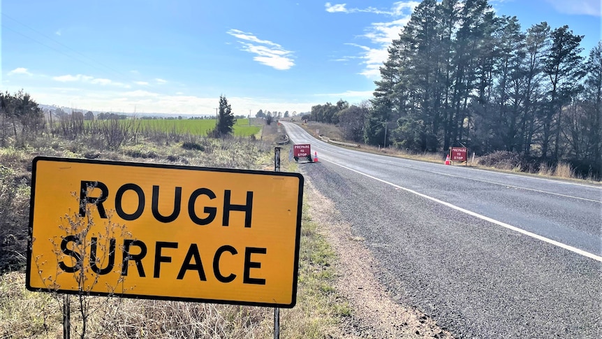 A stretch of road with a large sign saying ROAD SURFACE in the front.