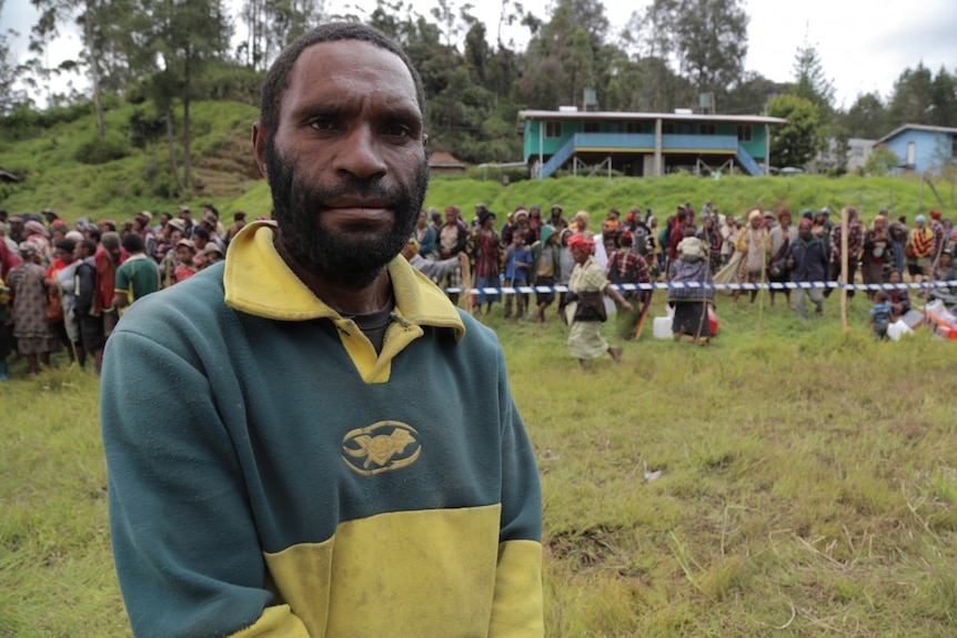 Man stands in front of a line of people waiting to receive aid in PNG