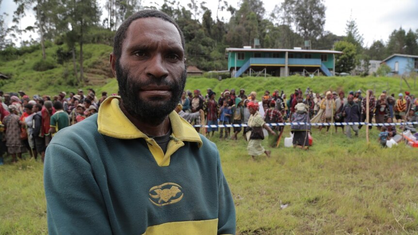 Man stands in front of a line of people waiting to receive aid in PNG