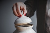 Woman lifting the lid of a funeral urn.
