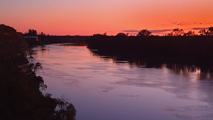 A wide river bending around a corner with orange skies overhead.