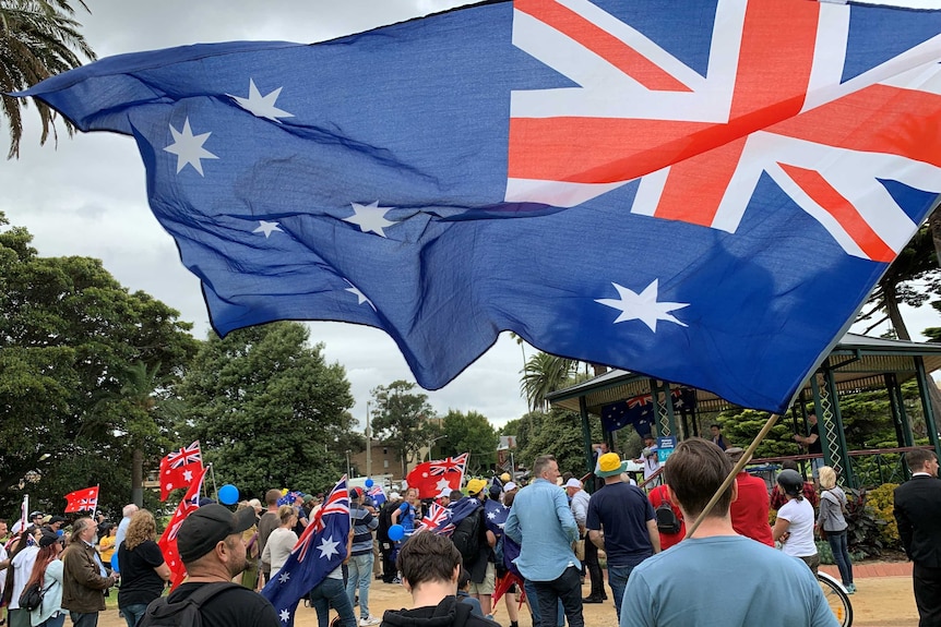 People fly Australian flags at a gathering in a park.