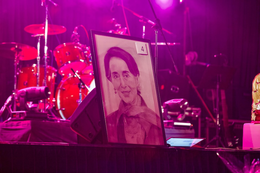 A framed portrait of a woman in a frame sits in front of a drum kit. 