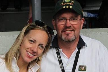 A young blonde woman leaning her head against a man wearing a white shirt and cap.