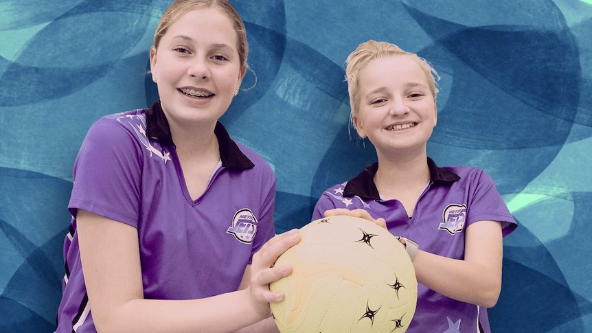 Two girls with their hands on the same netball pose for a photo.