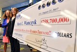 A woman stands next to a poster displaying her lottery winnings.