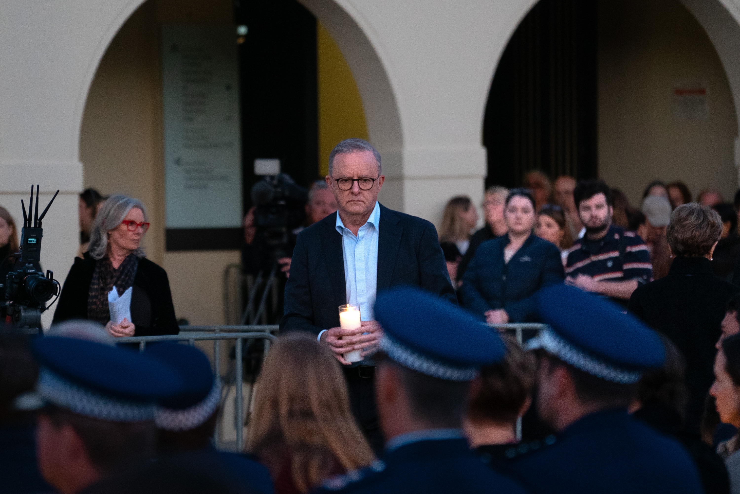 Anthony Albanese looks solemn as he walks in front of police officers with a lit candle.