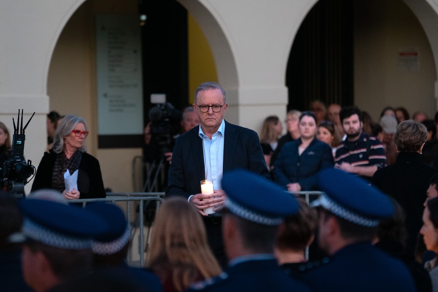 Anthony Albanese looks solemn as he walks in front of police officers with a lit candle.