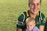 Mother in green football jersey holding baby after football match 