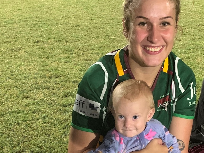 Mother in green football jersey holding baby after football match 