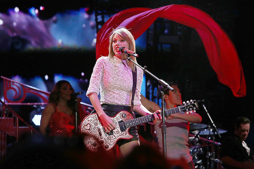 Blonde woman with guitar at microphone.