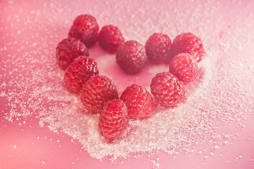 Red raspberries sitting in sugar crystals.