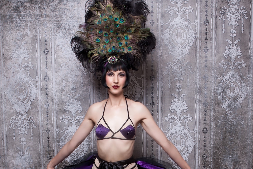 A'dora Derriere (Melanie Piantoni) wearing a burlesque costume and peacock feather head dress. 