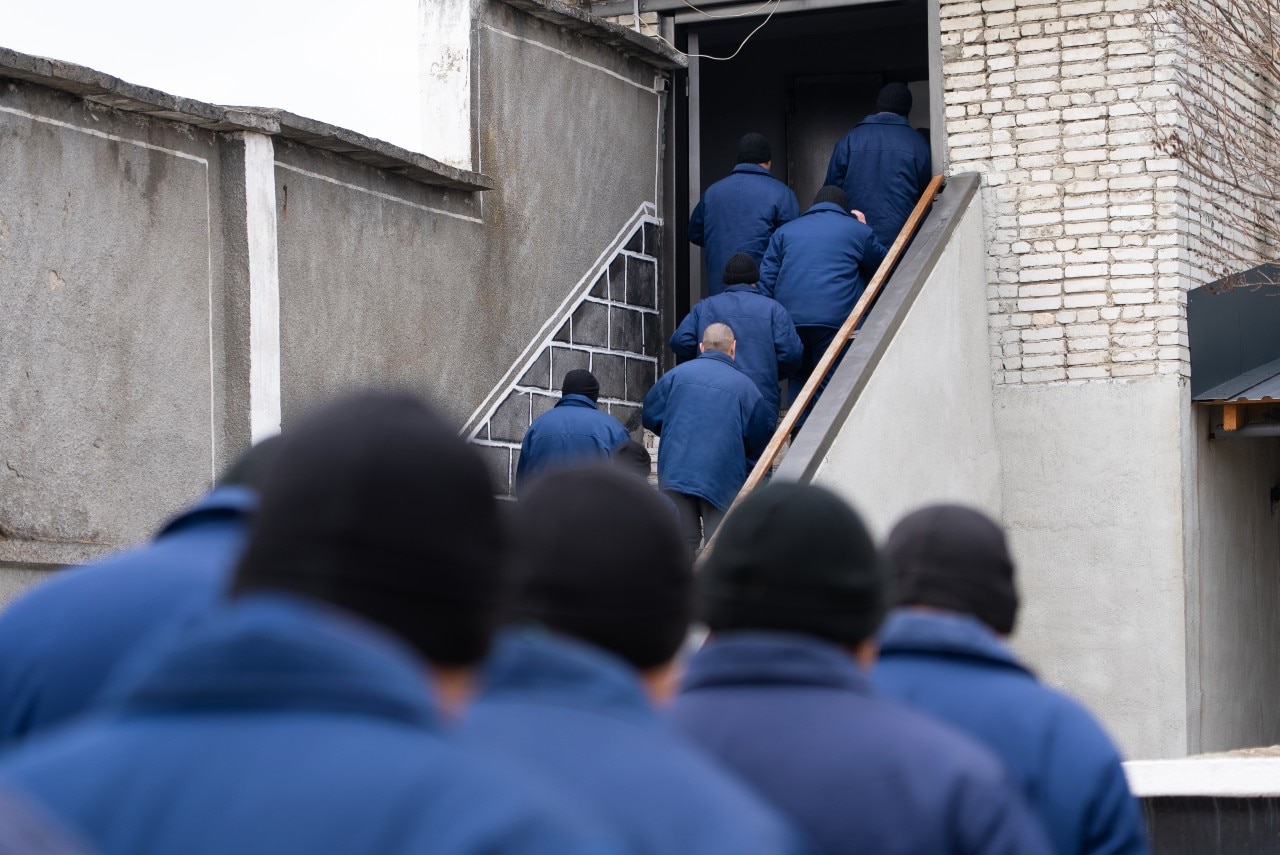A group of men wearing prison uniforms walking up stairs, seen from behind.