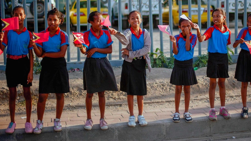 A group of little girls in school uniforms wave Timorese flags