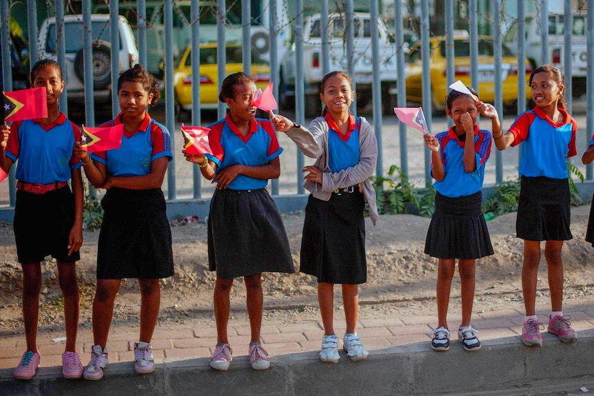 A group of little girls in school uniforms wave Timorese flags