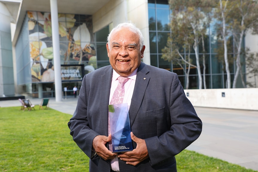 Tom Calma smiling holding a glass award