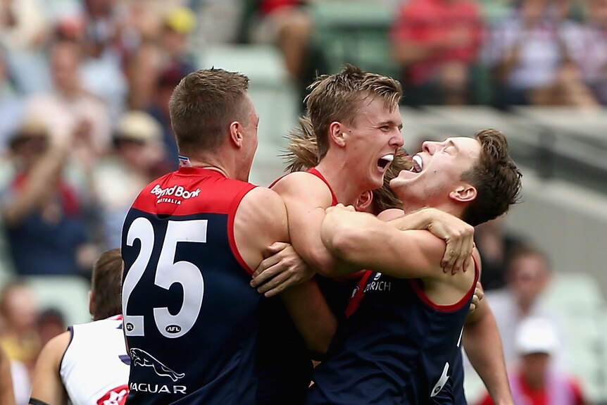Three Melbourne players jump and hug each other while smiling