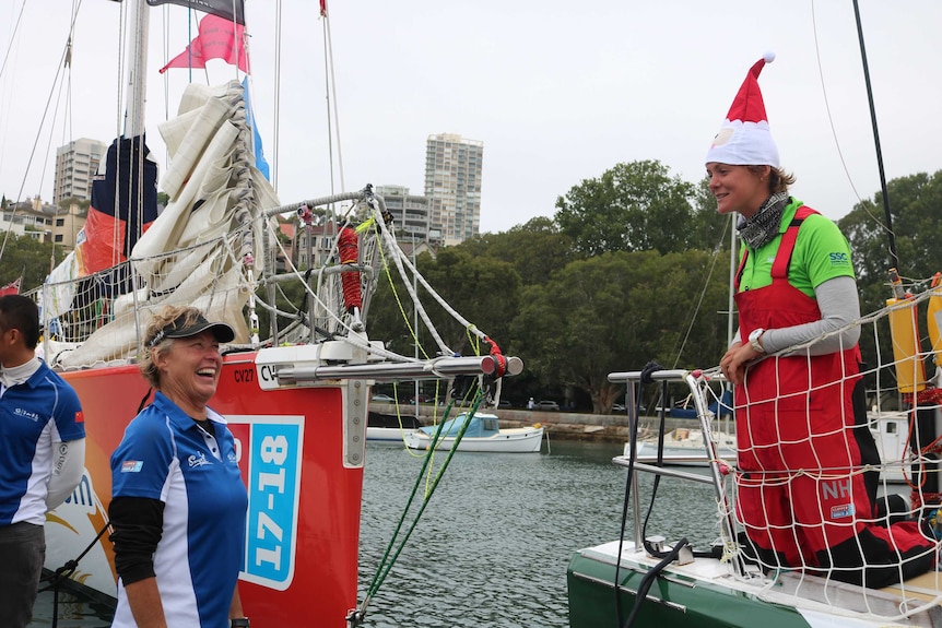 Wendy Tuck stands and looks up to Nikki Henderson standing in the bow of a yacht wearing a santa hat