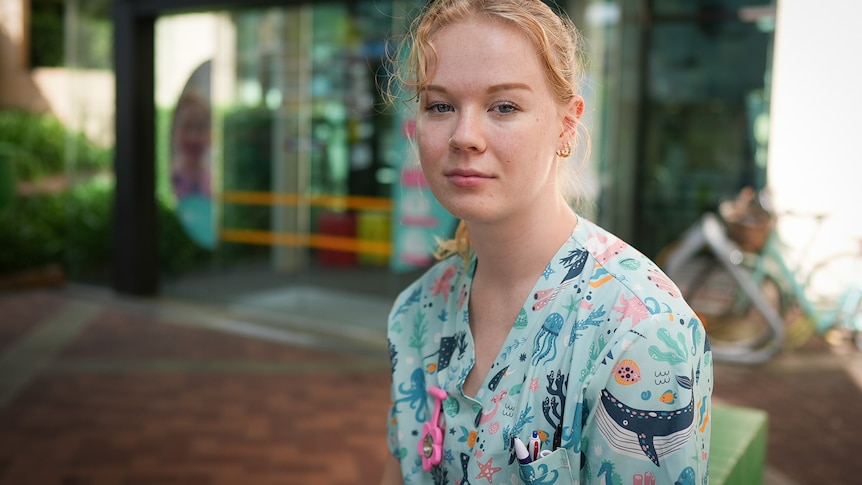 Victoria wears scrubs decorated with pictures of whales and other sea life, while sitting outside a hospital.