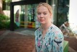 Victoria wears scrubs decorated with pictures of whales and other sea life, while sitting outside a hospital.