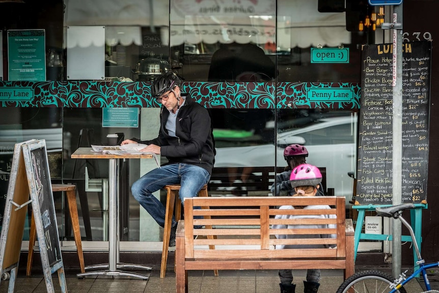 A man in a bicycle helmet sits at a cafe with a girl.